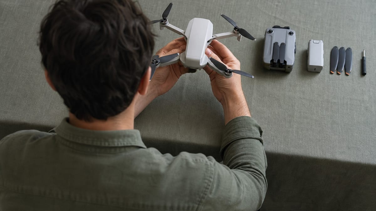 Mani che tengono un piccolo drone sopra un banco con radiocomando, batteria, eliche e cacciavite